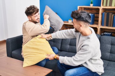 Young couple fighting with cushion sitting on sofa at home