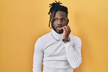 Sarı arka planda balıkçı yaka kazak giyen Afrikalı adam elleri ağız yiyen tırnaklarla gergin ve stresli görünüyor. anksiyete. 