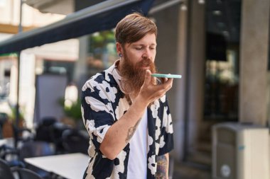 Young redhead man talking on the smartphone with serious expression at street