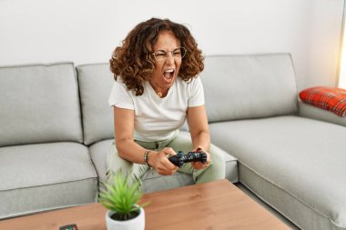 Evde kanepede oturmuş video oyunları oynayan olgun İspanyol bir kadın çığlık atıyor.