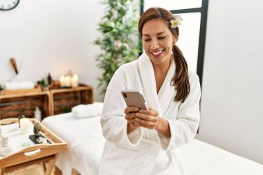 Young latin woman wearing bathrobe using smartphone 
