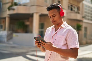 Young latin man using touchpad and headphones at street