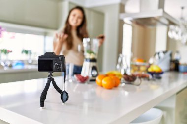 Genç ve güzel İspanyol kadın, mutfakta kamerayla blender ile sebze kokteyli hazırlıyor.