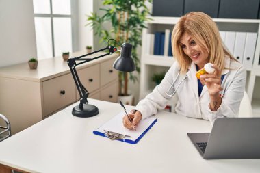 Middle age blonde woman wearing doctor uniform prescribe pills at clinic