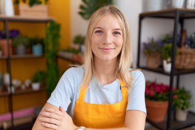 Young blonde woman florist smiling confident sitting on table at flower shop