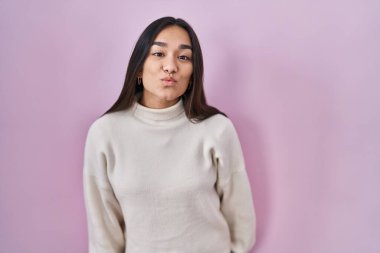Young south asian woman standing over pink background looking at the camera blowing a kiss on air being lovely and sexy. love expression. 