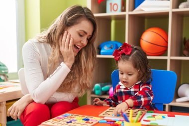 Teacher and toddler playing with maths puzzle game sitting on table at kindergarten