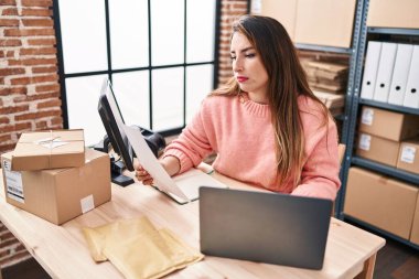 Young beautiful hispanic woman ecommerce business worker using laptop reading paperwork at office