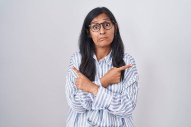 Young hispanic woman wearing glasses pointing to both sides with fingers, different direction disagree 