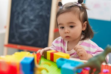 Adorable chinese toddler playing with construction blocks standing at kindergarten