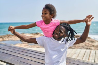 Father and daughter smiling confident holding girl on back at seaside
