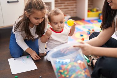 Erkek ve kız kardeş anaokulunun zemininde oturmuş inşaat bloklarıyla oynuyorlar.