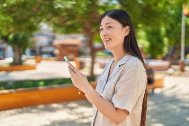 Parkta akıllı telefon kullanan, kendine güvenen Çinli bir kadın.