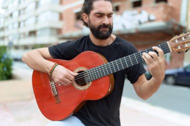 Young hispanic man musician playing classical guitar at street