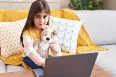 Adorable hispanic girl using laptop sitting on sofa at home
