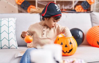 Adorable hispanic boy having halloween party holding pumpkin basket at home