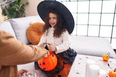 Adorable hispanic girl wearing halloween costume holding pumpkin basket at home