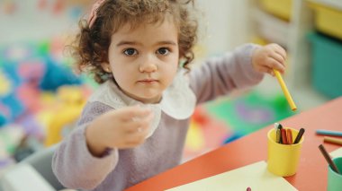 Adorable hispanic girl preschool student sitting on table drawing on paper at kindergarten