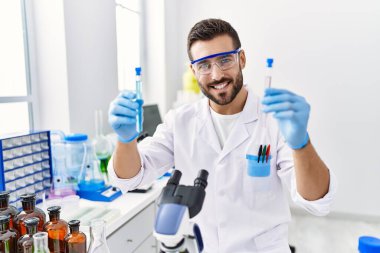 Laboratuvarda deney tüpü tutan bilim adamı üniforması giyen İspanyol genç adam.