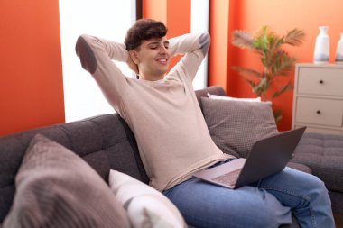 Non binary man using laptop relaxed on sofa at home