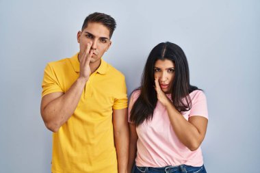 Tecrit edilmiş arka planda duran genç bir çift. Ağızlarına el sürerek gizli dedikodular fısıldıyor, kötü niyetli konuşmalar yapıyor. 