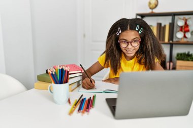 Afro-Amerikalı kız gülümseyerek evde ödevini yapıyor.