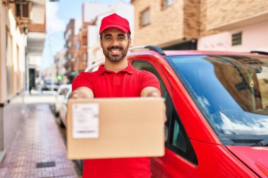 Genç İspanyol kurye sokakta paket tutuyor.