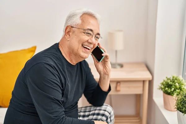 Senior man talking on the smartphone sitting on bed at bedroom