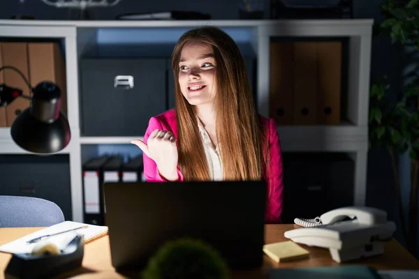 年轻的高加索女人 晚上在办公室工作 面带微笑 面带微笑 手指头指向旁边 — 图库照片