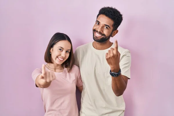 Young Hispanic Couple Together Pink Background Beckoning Come Here Gesture — Stok fotoğraf