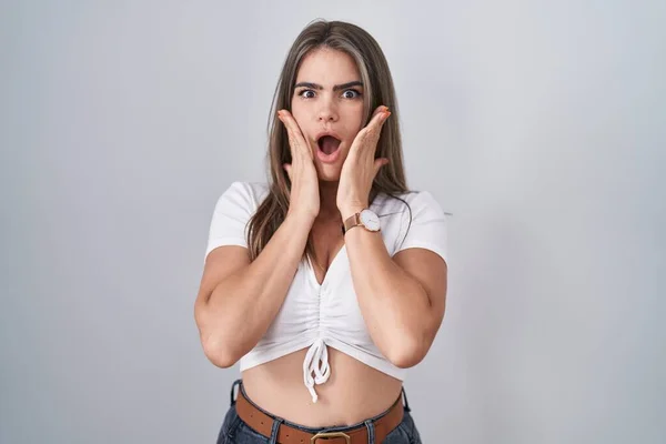 Young beautiful woman wearing casual white t shirt afraid and shocked, surprise and amazed expression with hands on face