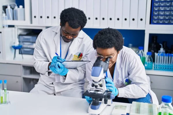 アフリカ系アメリカ人の男性と女性の科学者は 実験室で文書に顕微鏡を使って — ストック写真