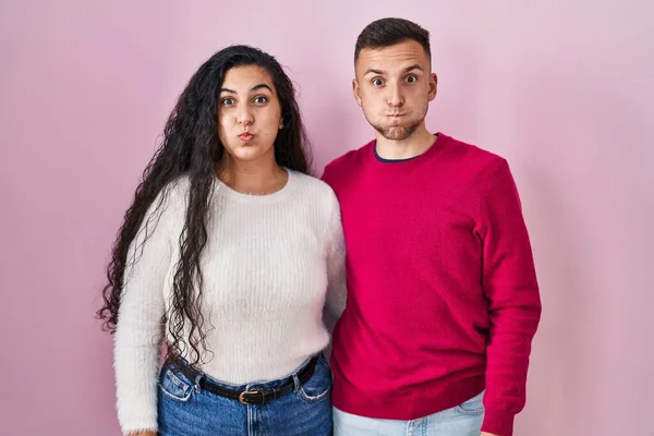 Young Hispanic Couple Standing Pink Background Puffing Cheeks Funny Face — Stockfoto