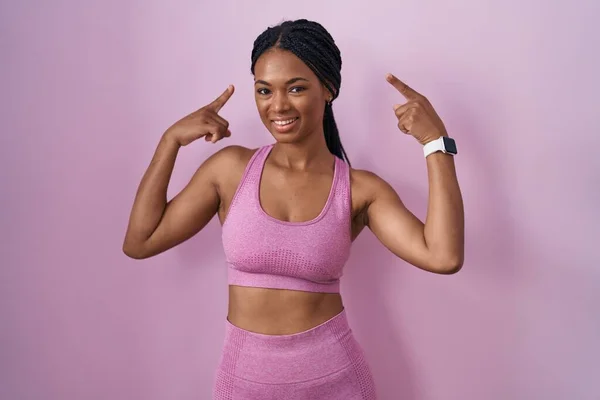 African American Woman Braids Wearing Sportswear Pink Background Smiling Pointing — Zdjęcie stockowe