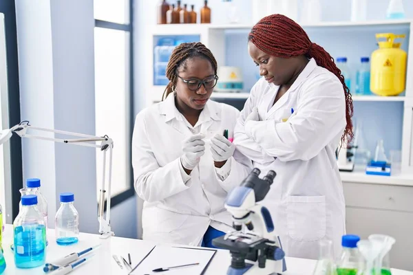 African american women scientists looking sample standing with arms crossed gesture at laboratory