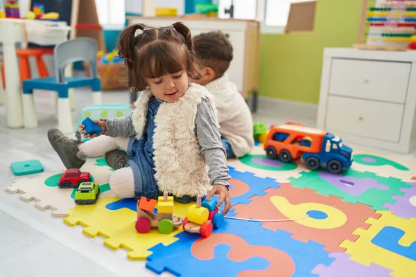 Brother and sister playing with cars toy sitting on floor at kindergarten