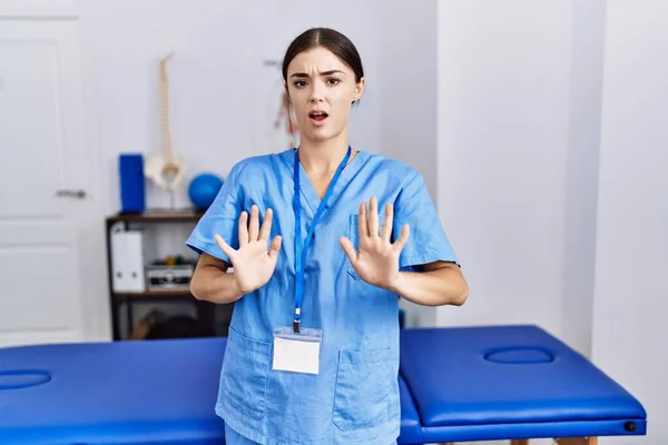 理学療法士を身に着けている若いヒスパニック系の女性は 恐怖と嫌な表情で拒否と否定を示す手のひらを離れて移動診療所に立って制服を着ています 止めて禁止する — ストック写真