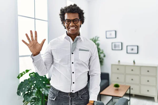 African psychologist man at consultation office showing and pointing up with fingers number five while smiling confident and happy.