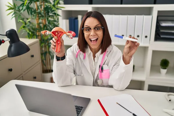 Young hispanic doctor woman holding anatomical model of female genital organ and pregnancy test celebrating crazy and amazed for success with open eyes screaming excited.