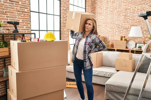 Young blonde woman holding heavy package at new home