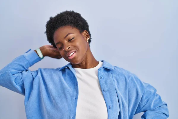 African american woman standing over blue background stretching back, tired and relaxed, sleepy and yawning for early morning