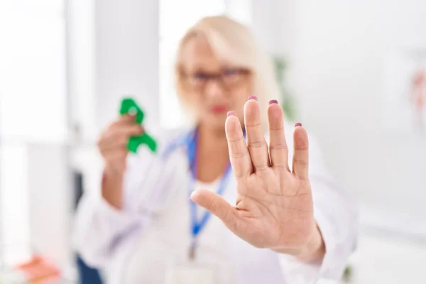 Middle age caucasian woman holding support green ribbon with open hand doing stop sign with serious and confident expression, defense gesture