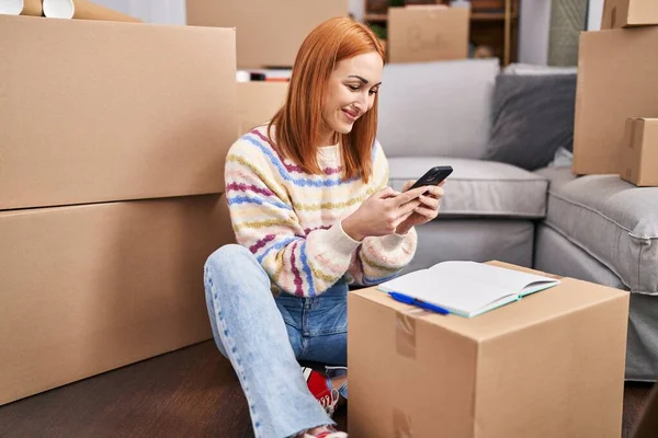 Young caucasian woman using smartphone sitting on floor at new home