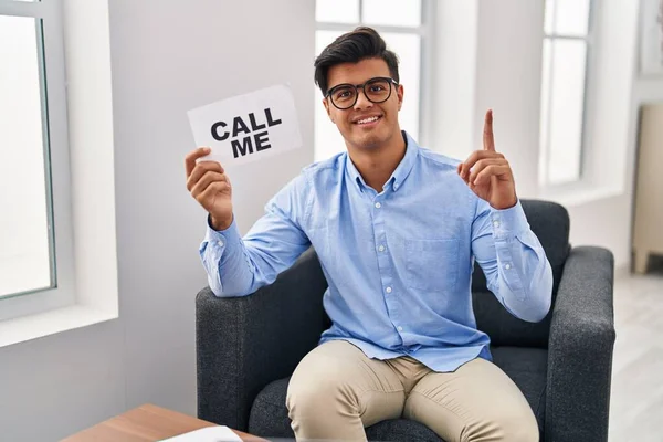 Hispanic man working at therapy office holding call me banner surprised with an idea or question pointing finger with happy face, number one