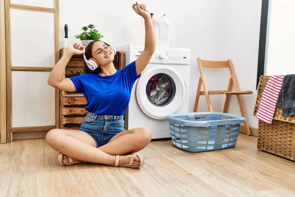 洗濯室で洗濯機を待っている音楽を聞いている若い白人女性 — ストック写真