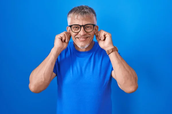 Hispanic Man Grey Hair Standing Blue Background Smiling Pulling Ears — Stockfoto