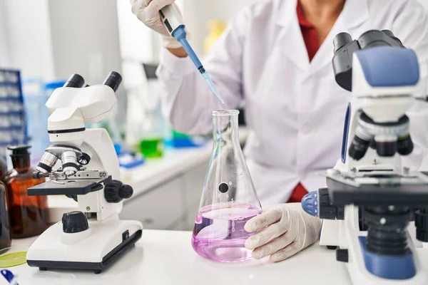 Laboratuvarda pipet kullanan orta yaşlı İspanyol kadın bilim adamı üniforması giyiyor.