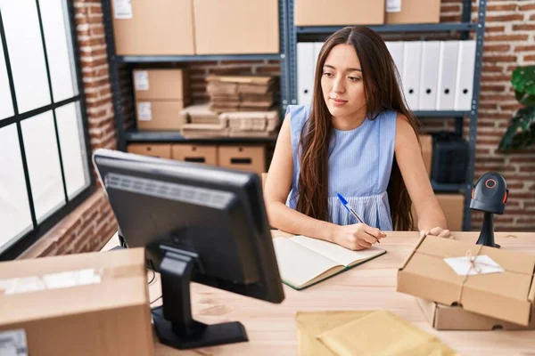 Young beautiful hispanic woman ecommerce business worker using computer writing on notebook at office