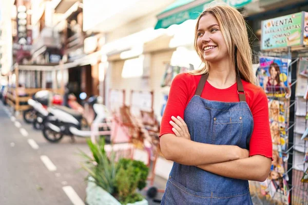 Young hispanic woman shop assistant standing with arms crossed gesture at street