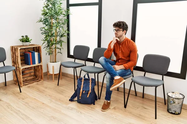 Young hispanic man boring sitting on chair at waiting room
